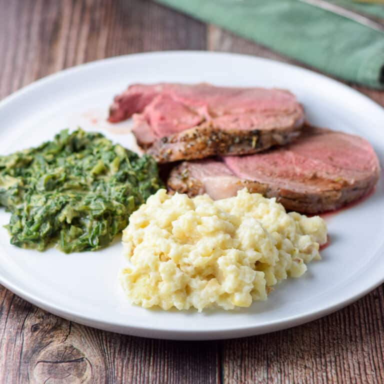 A plate of mashed root with spinach and slices of lamb - square