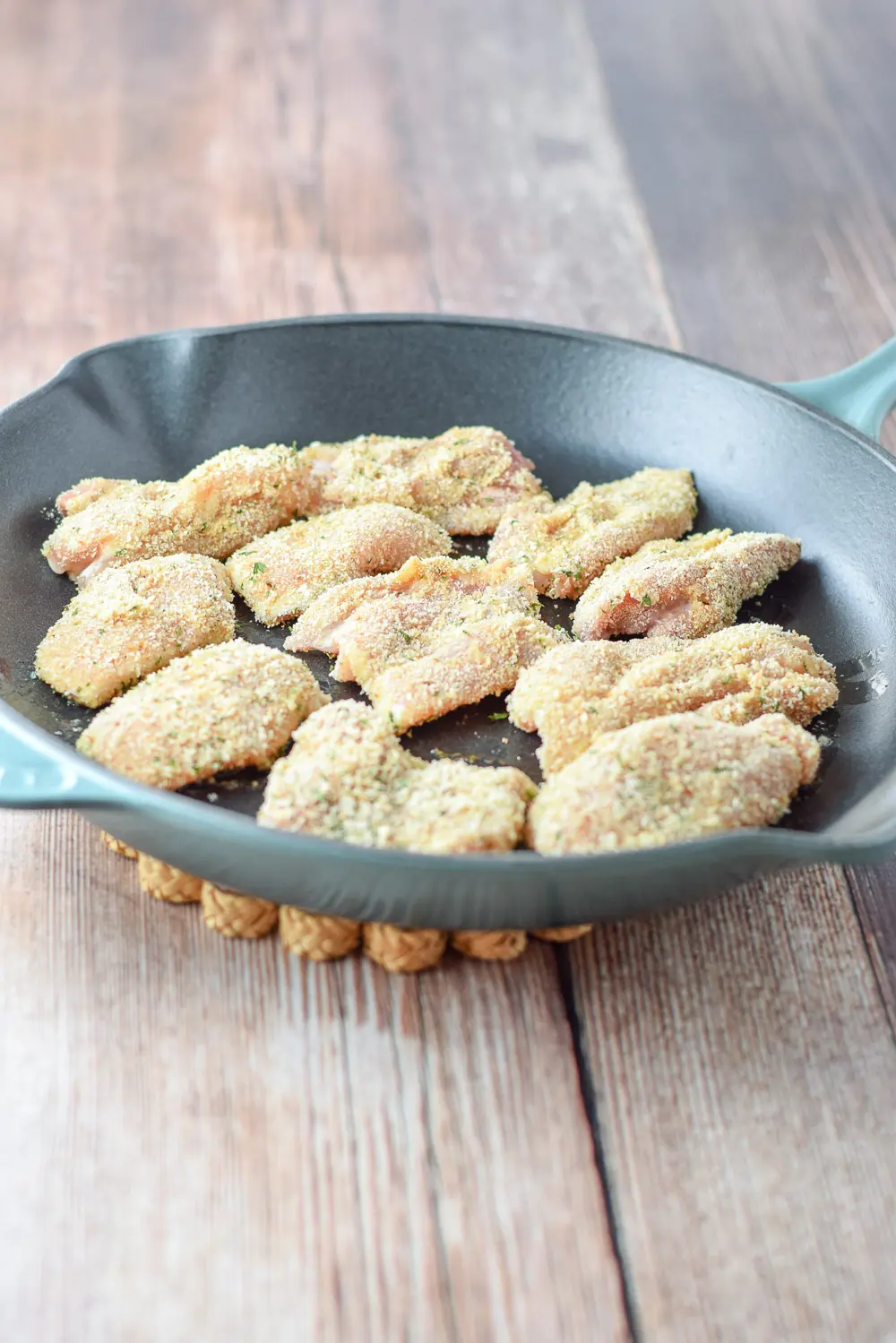 Breaded raw chicken in a cast iron pan
