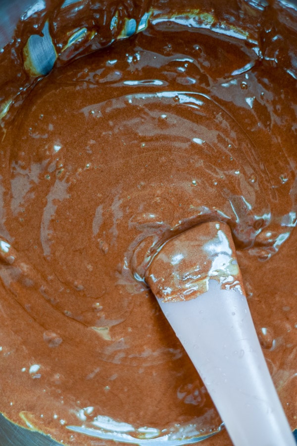 The whipped yolks added to the melted chocolate with a pink spatula in a metal bowl