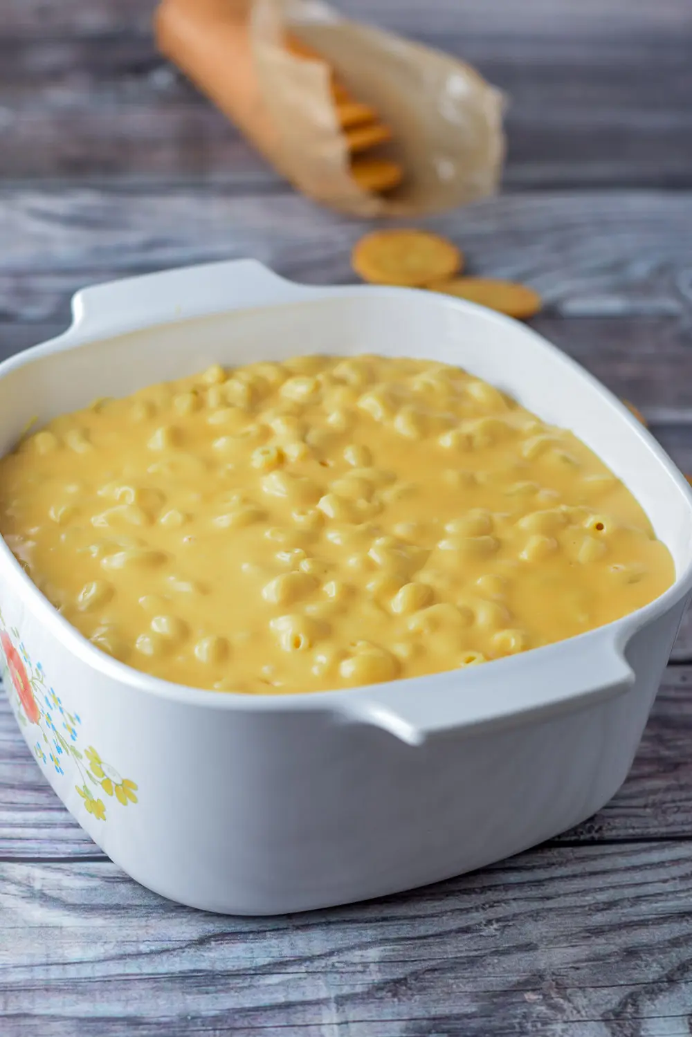Elbow macaroni and cheese sauce in a casserole dish with some Ritz crackers in the background