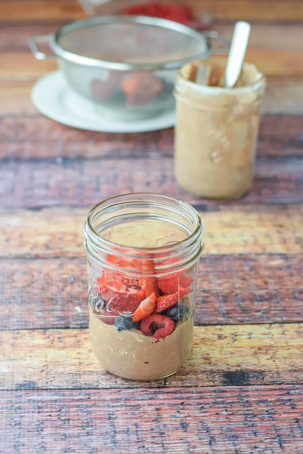 A layer of overnight oats with fruit on top. There is another jar of the oats and more fruit in the background