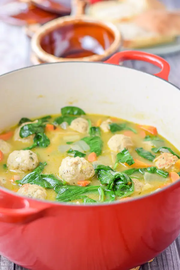 A red Dutch oven filled with a soup with meatballs and spinach in it