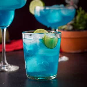 vertical view of the three glasses of the blue drink with a plant in the background - square