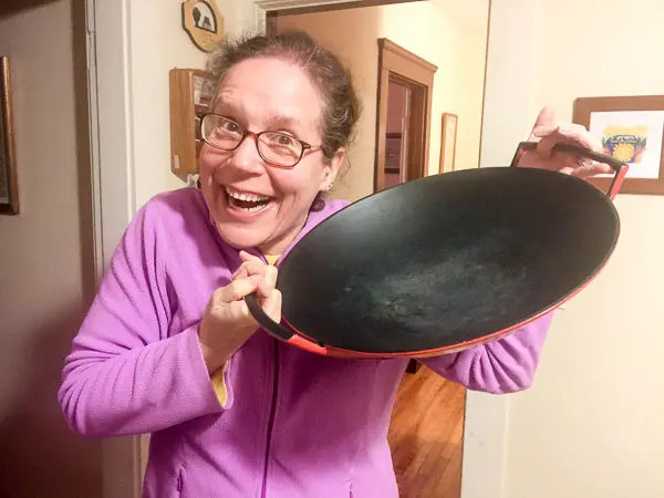 Elaine, wearing a wide, goofy smile and holding up her red Le Creuset wok, purchased at a local Savers thrift store.