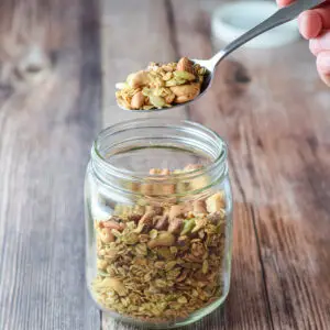 A hand holding a spoon of granola over the jar - square