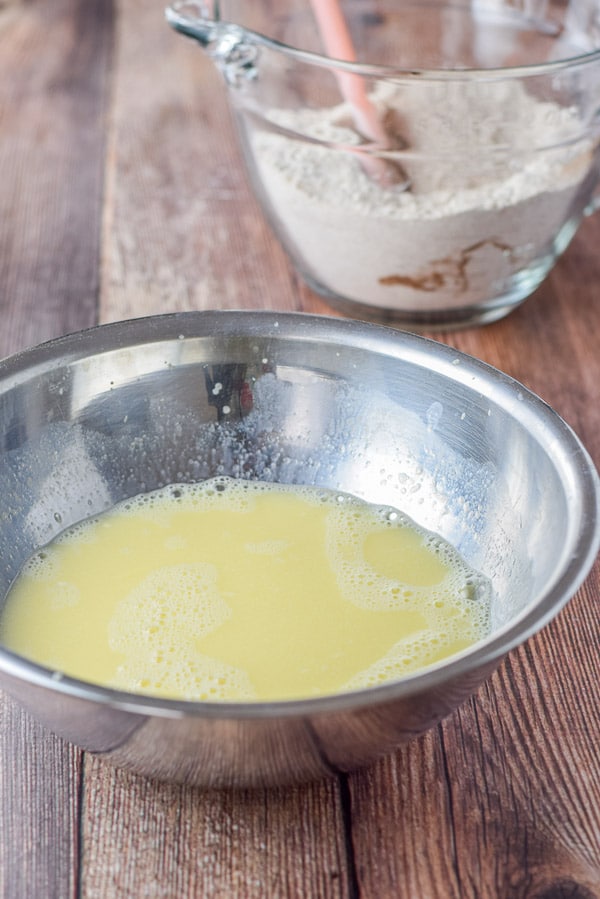 A silver bowl with the egg and milk whisked and the dry ingredients in the background