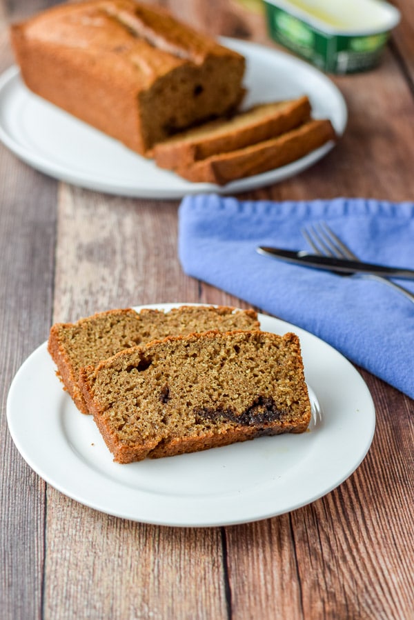 Two slices of bread on a small white plate with the rest of the bread on a bigger plate in the background