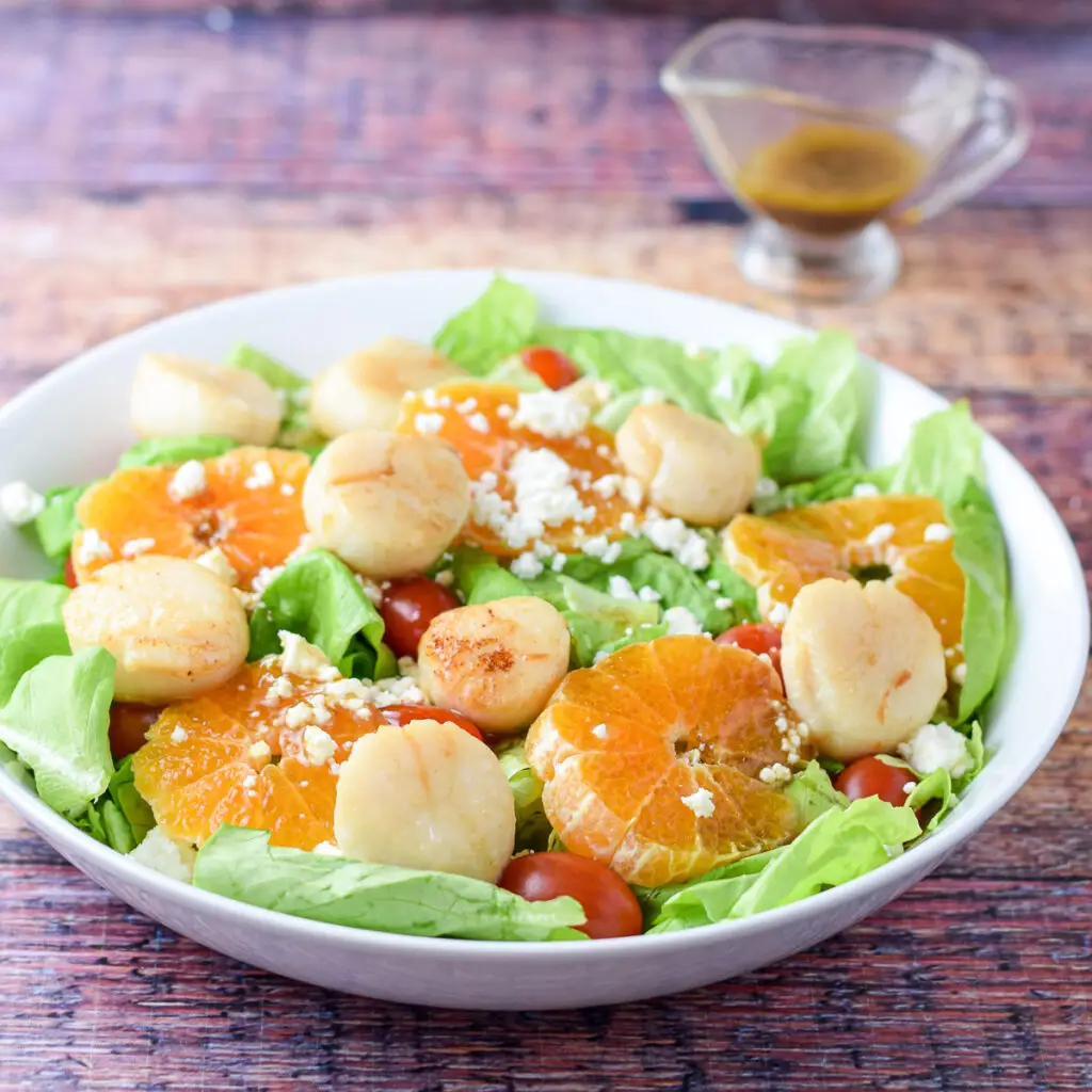 Dressing poured for on the salad with orange slices and scallops - square