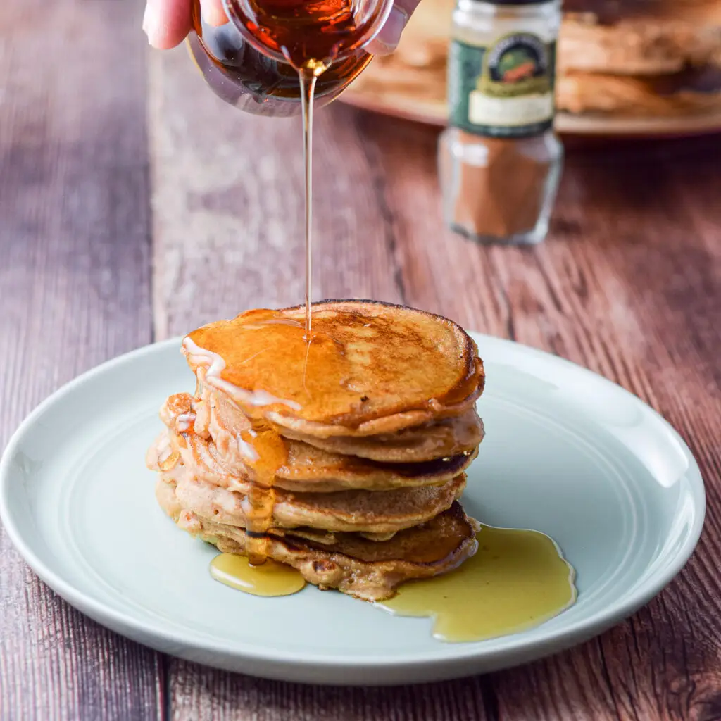 A green plate piled with pancakes and then drizzled with maple syrup - square
