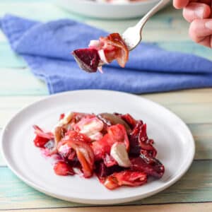 A male hand holding a forkful of beet salad over a white plate - square