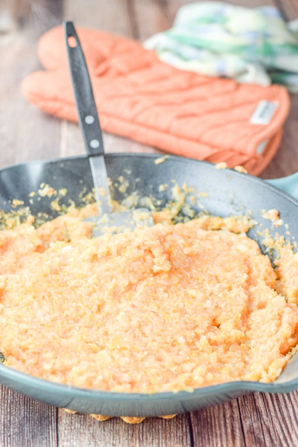 Vegetables cooked in a green cast iron pan with a spatula in it