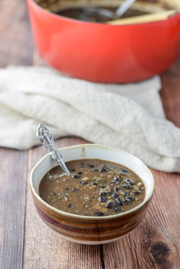 A brown bowl og bean soup with a spoon in it and the pan in the background
