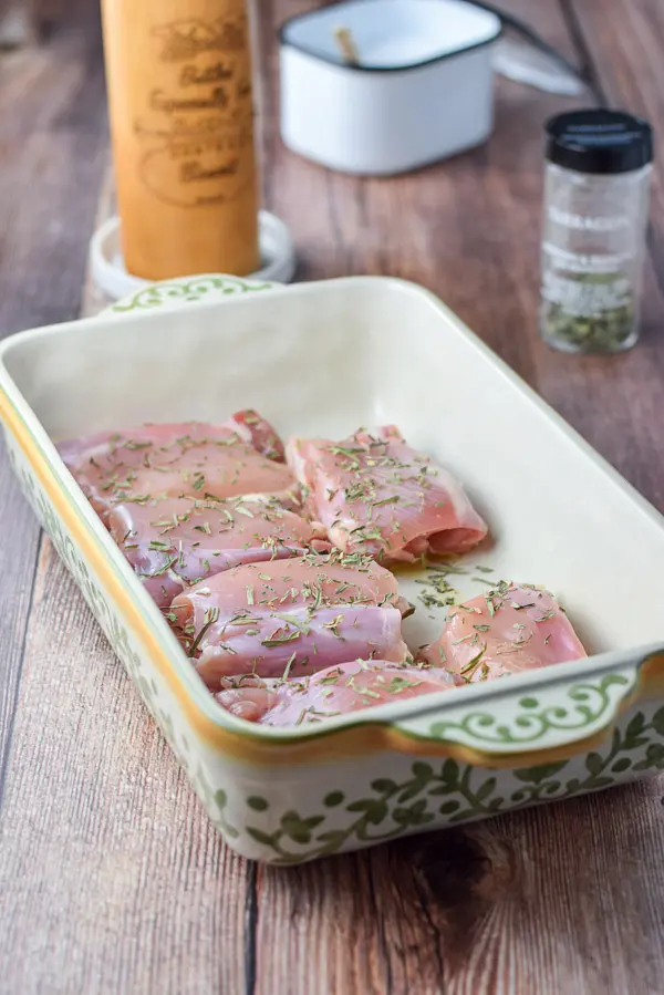 A baking dish with chicken thighs with tarragon, salt and pepper on top