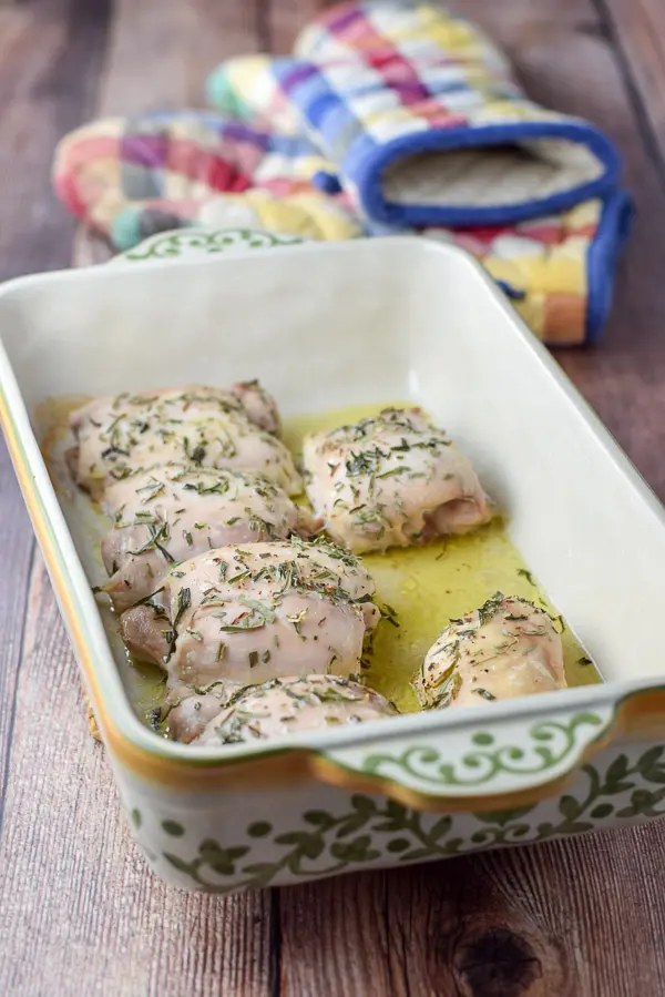 A baking dish with chicken baked with tarragon on it and two oven mitts in the background