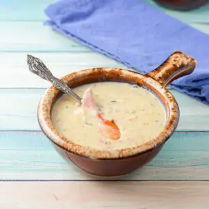 A spoon in the bowl of bisque with lobster claw meat in it - square