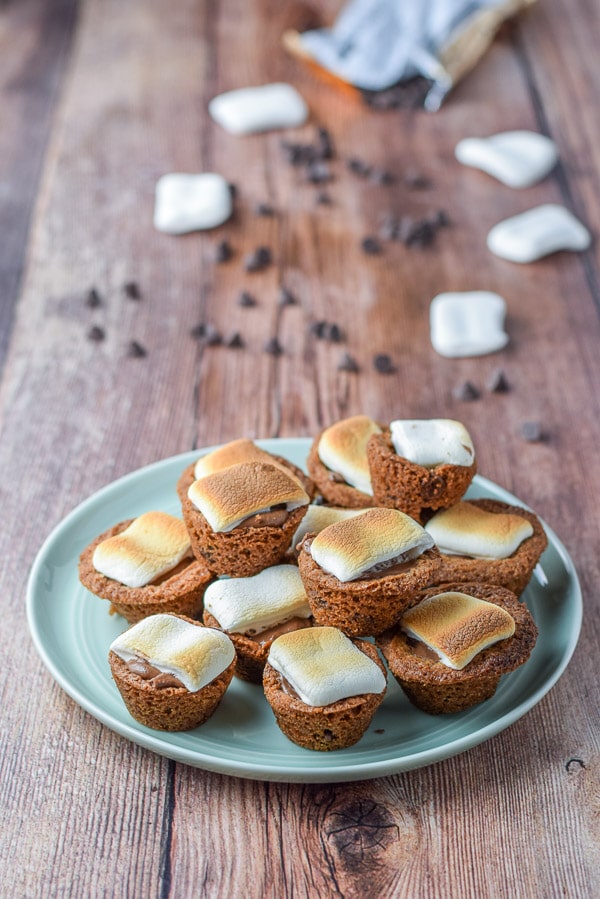 A green plate piled with little muffin cookies with marshmallows on the table along with chocolate chips