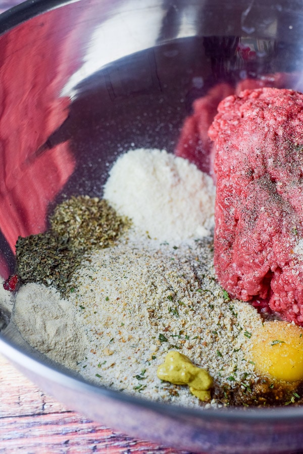 Beef and herbs and spices, egg, cheese and bread crumbs in a bowl