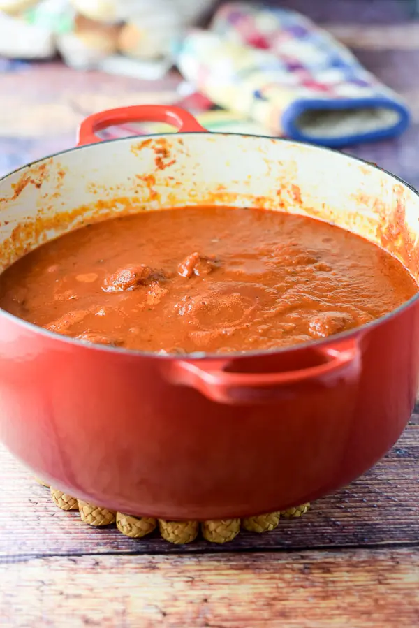 A red Dutch oven filled with cooked marinara and meatballs added to it