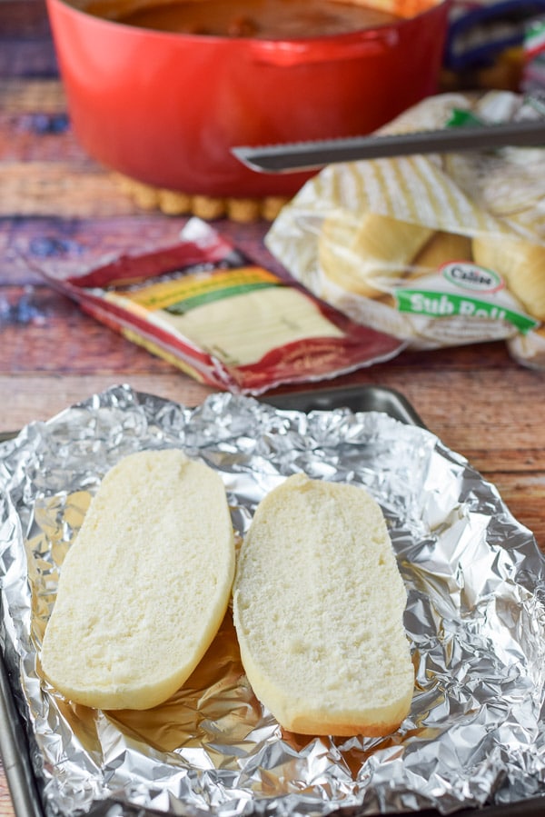 Bread cut and placed on a foil lined pan with cheese and the sauce in the background