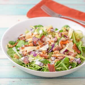 A deep white bowl with the salad in it and a napkin and fork in the background - square