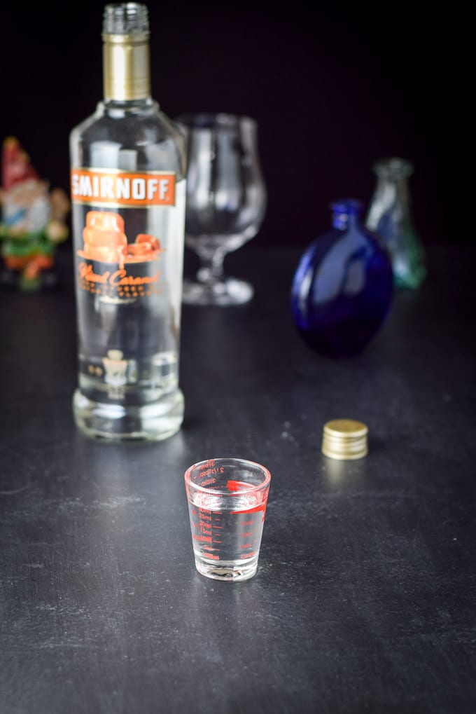 Caramel vodka poured out with the bottle and glasses in the background