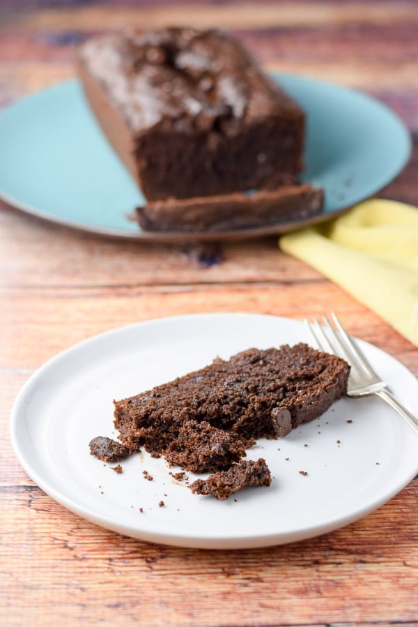 A piece of chocolate bread with a bite taken out with the bread in the background on a blue plate