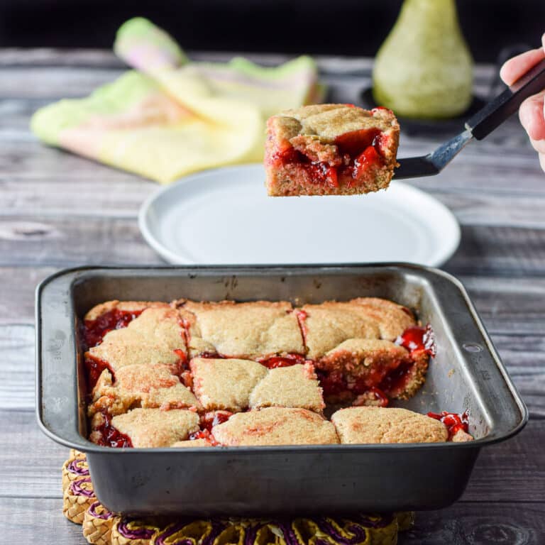 A hand holding a spatula with a piece of the cherry dessert held over the pan - square