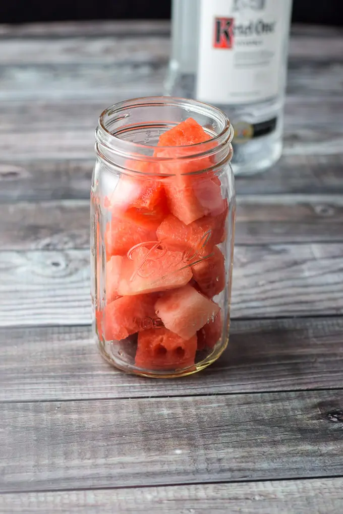 Watermelon chunks in a jar with the bottle of vodka in the background