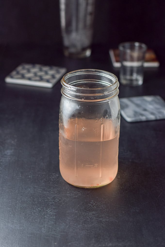 Watermelon taken out of the jar leaving the pink vodka. There are coasters, a measuring glass and shaker in the background