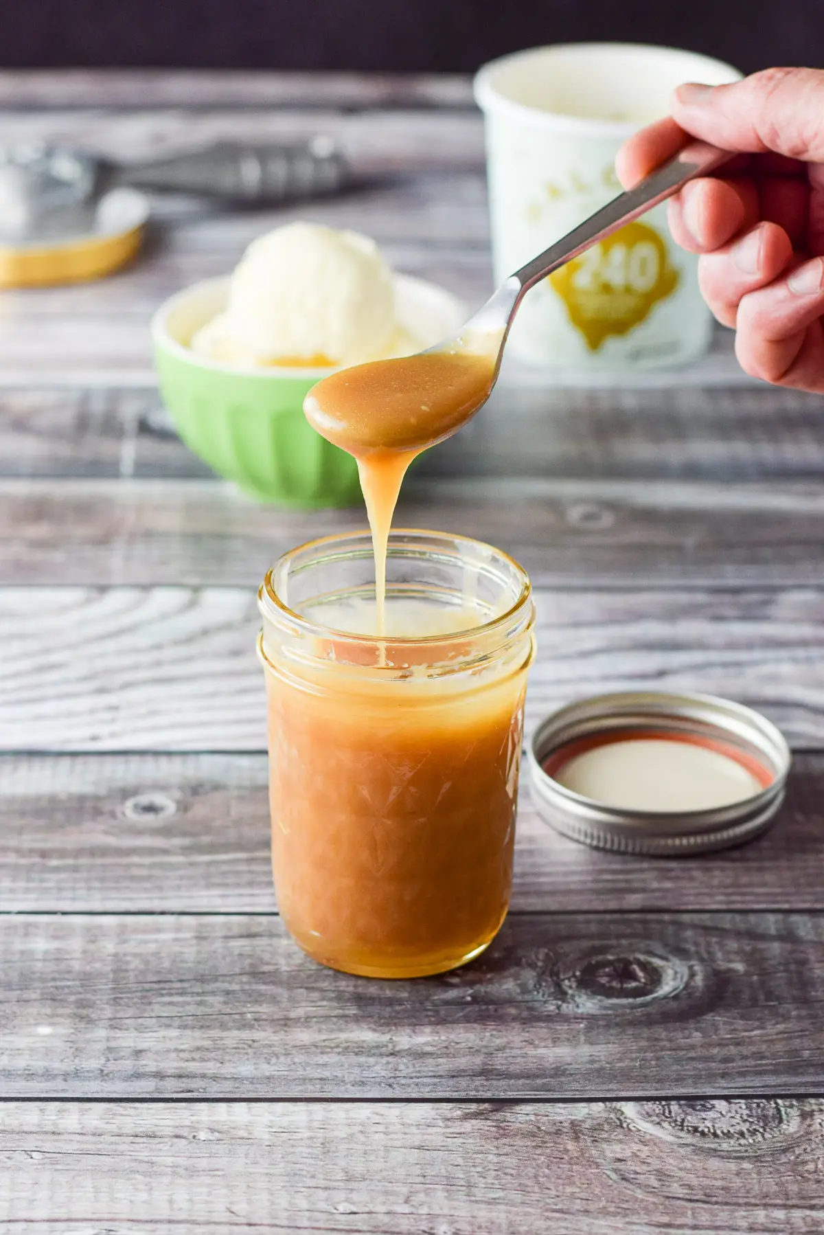 Spoonful of the caramel sauce held over the jar with ice cream in the background