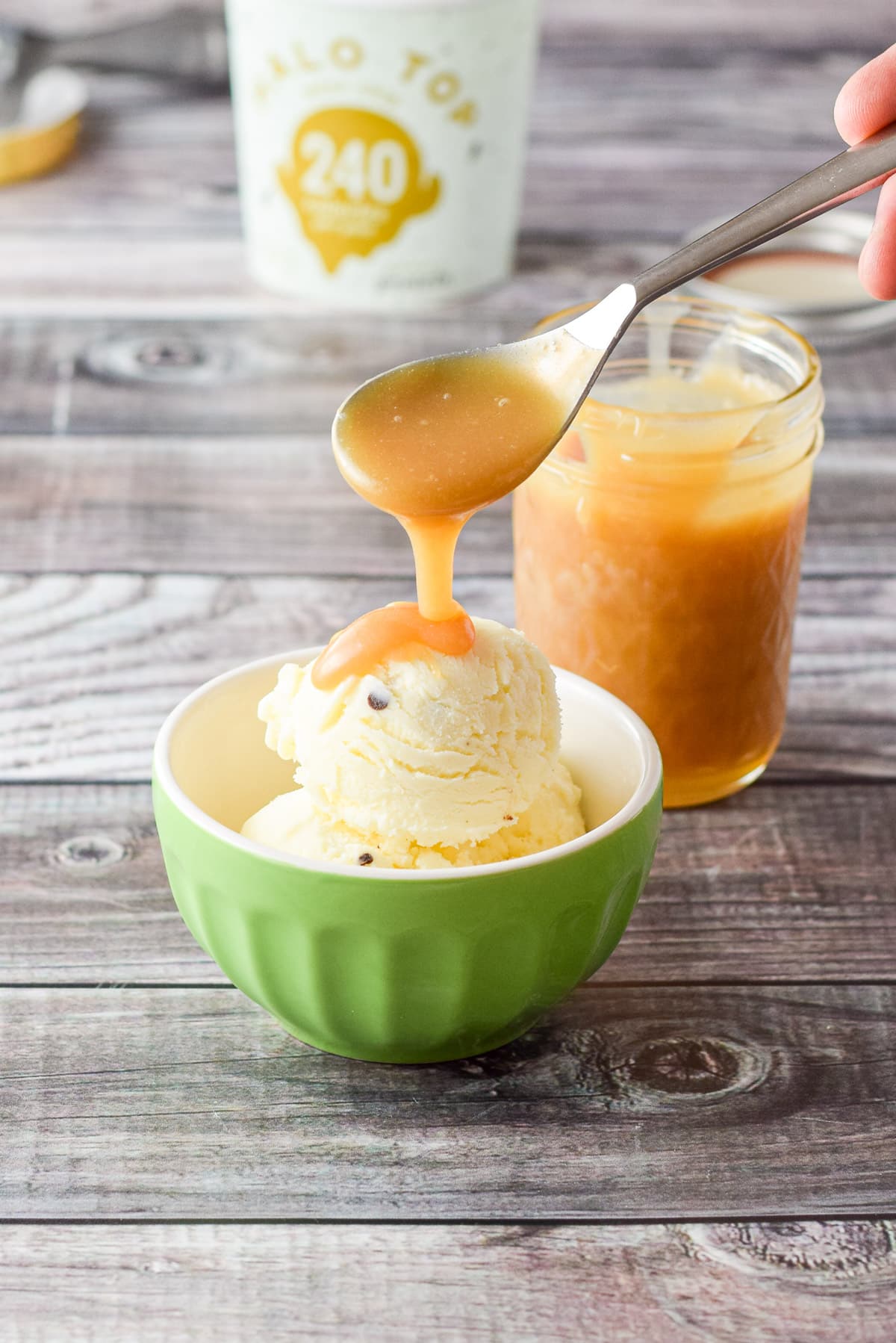 A hand pouring caramel sauce onto ice cream in a green bowl