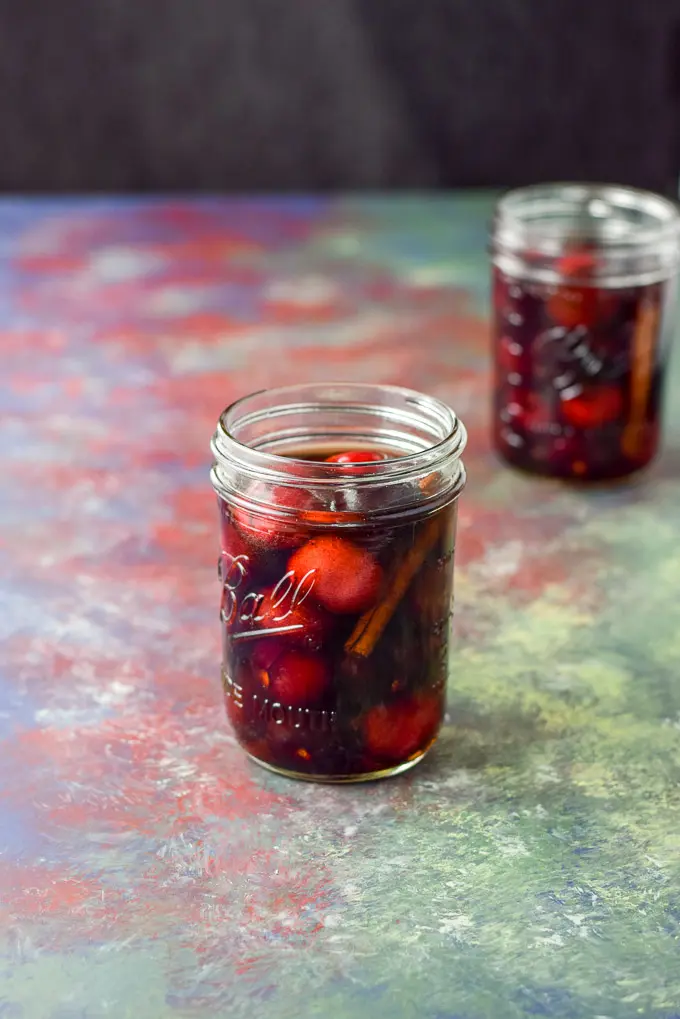 Two jars of cherries soaked in bourbon on a colorful table