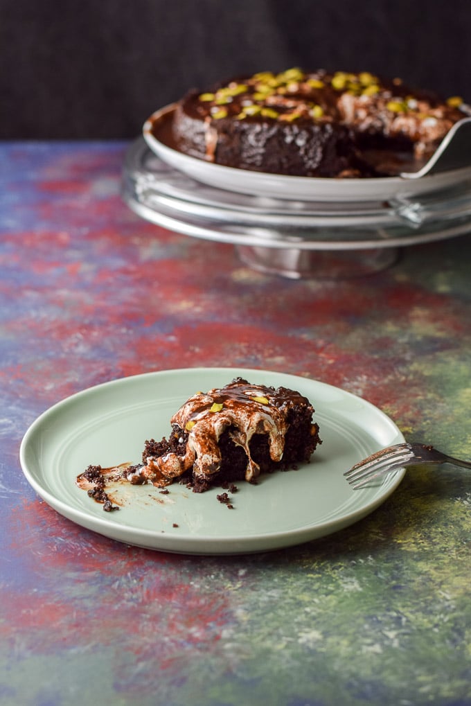 a forkful of cake missing from the piece on a green plate. The pedestal with the cake in the background