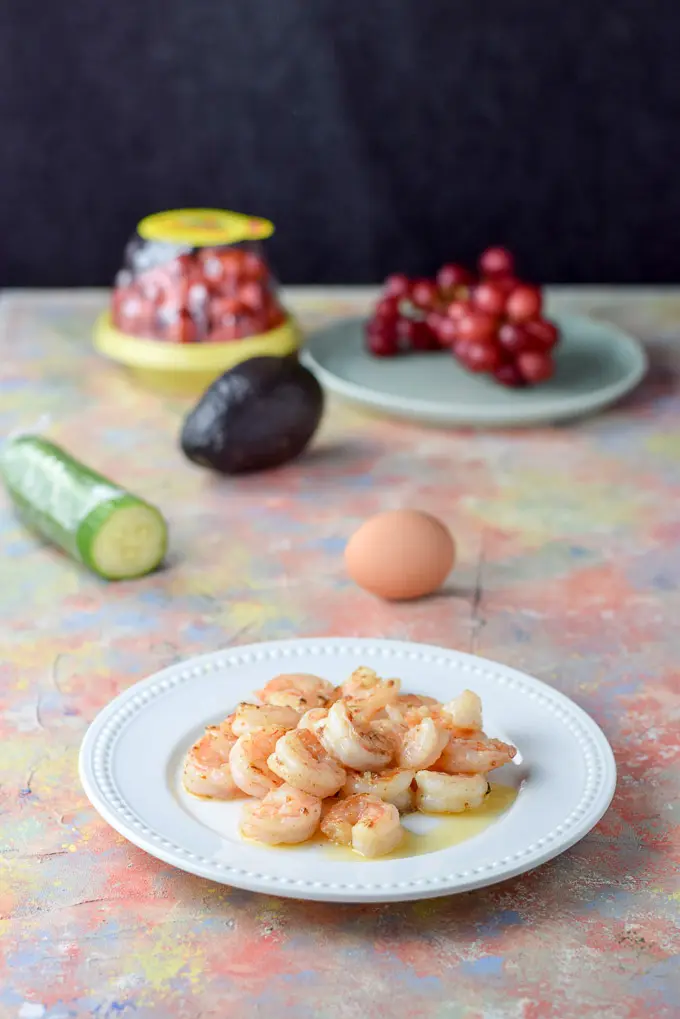 Sauted shrimp, egg, cucumber, tomatoes and grapes on a colorful table