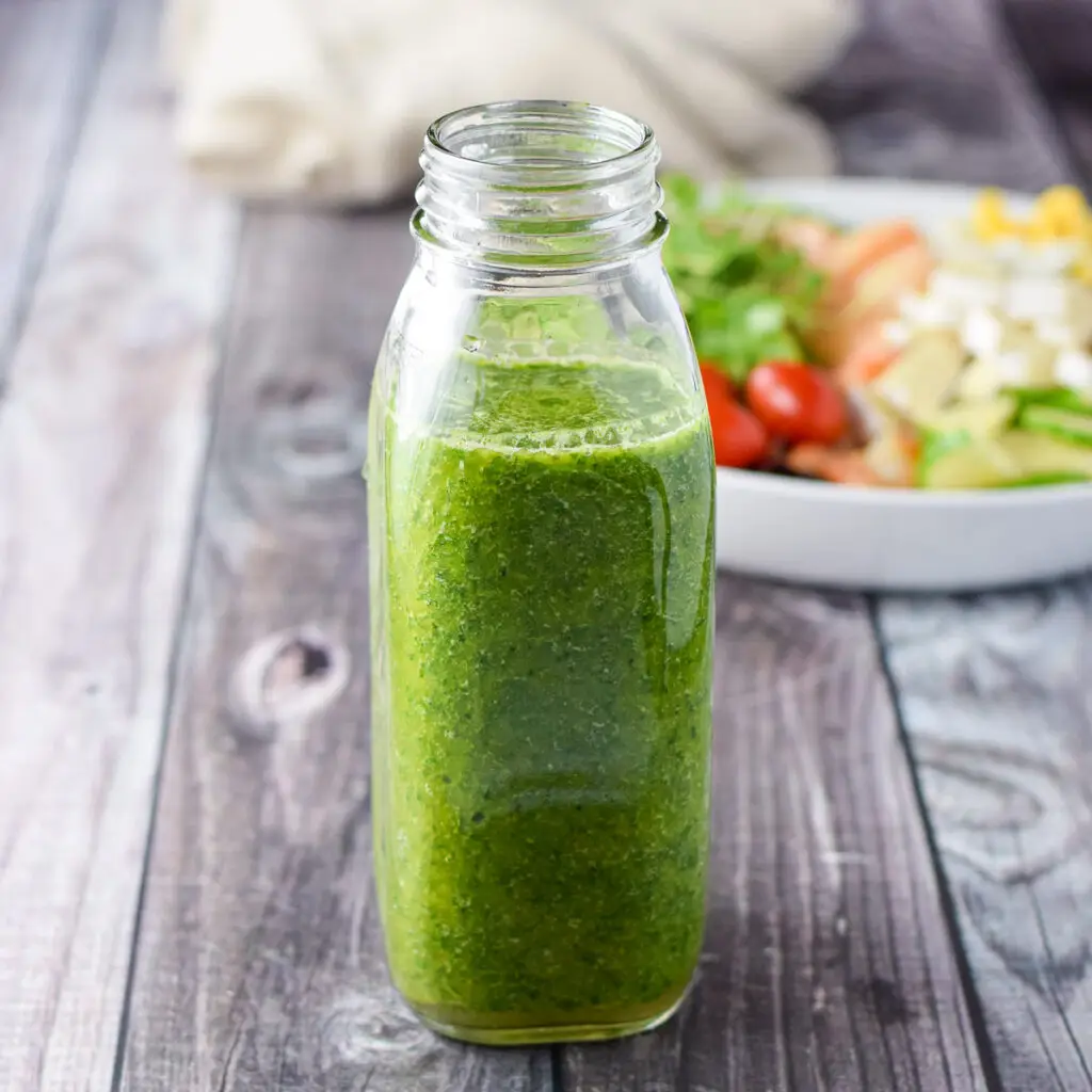 A bottle filled with the green dressing with a salad in the background