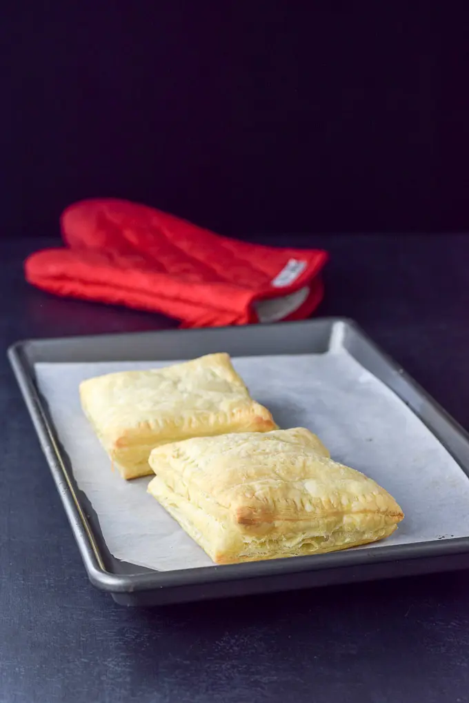 A jelly roll pan with two golden puff pastry squares stuffed with cream cheese and rhubarb sauce