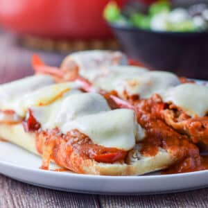 A vertical view of a white plate with the bread covered with sausage, veggies, gravy and melted cheese - square