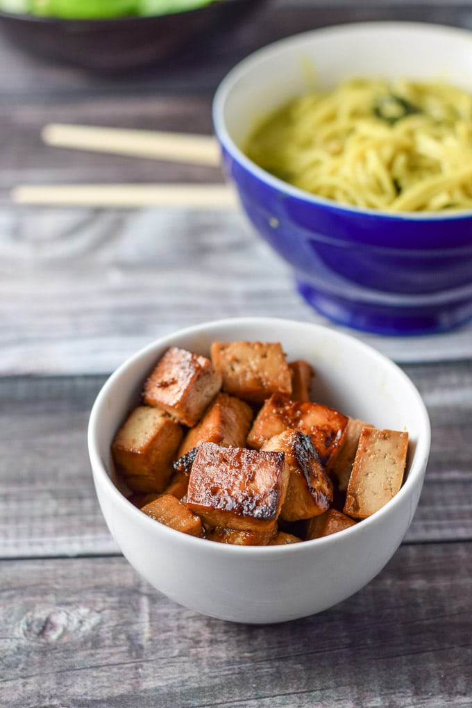 A white bowl with saut&eacute;ed tofu with a bowl of noodles in the background