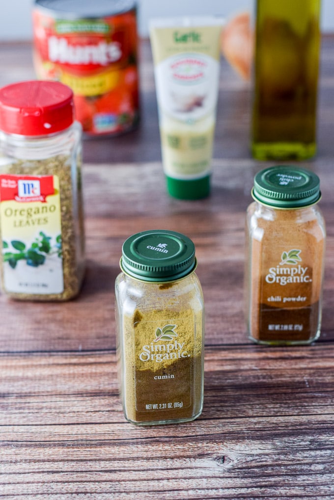 Cumin, chili powder, oregano, garlic past, diced tomatoes, oil and an onion on the table