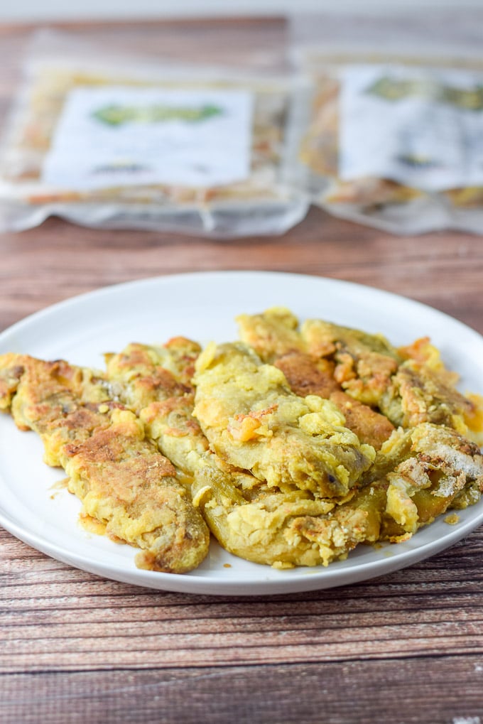 Rellenos battered and fried on a white plate with packages of chiles in the background