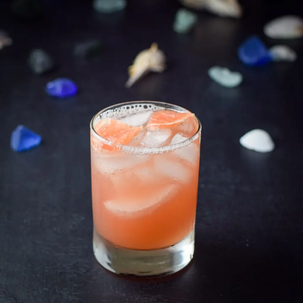 a peach colored cocktail in a double old fashioned glass with chunks of grapefruit in the background - square