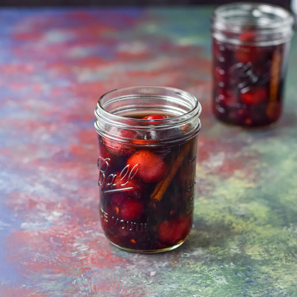 Cherries and cinnamon in bourbon in two jars on a table - square