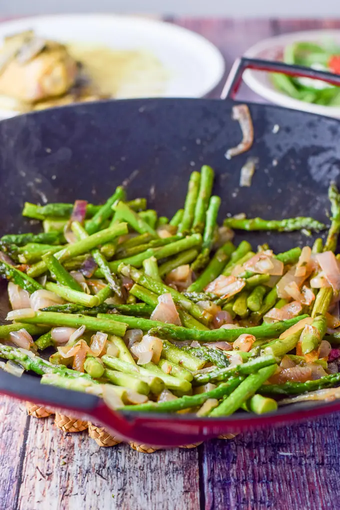 Asparagus in the wok completely cooked with a plate of chicken in the background