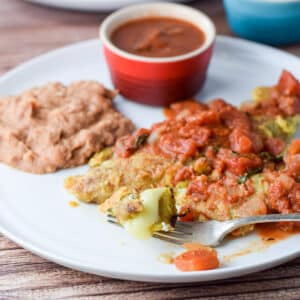 A fork with some chile relleno on it with beans and enchilada sauce - square