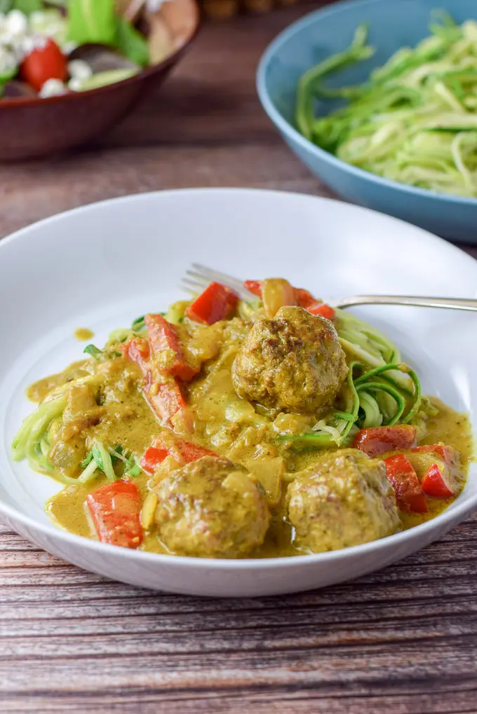 A white shallow bowl with meatballs in curry sauce over zoodles