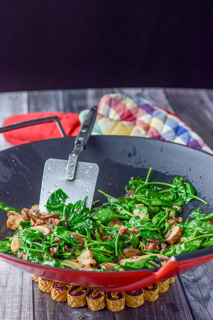 Spinach, pancetta and mushrooms sautéed in a red wok with a spatula in it
