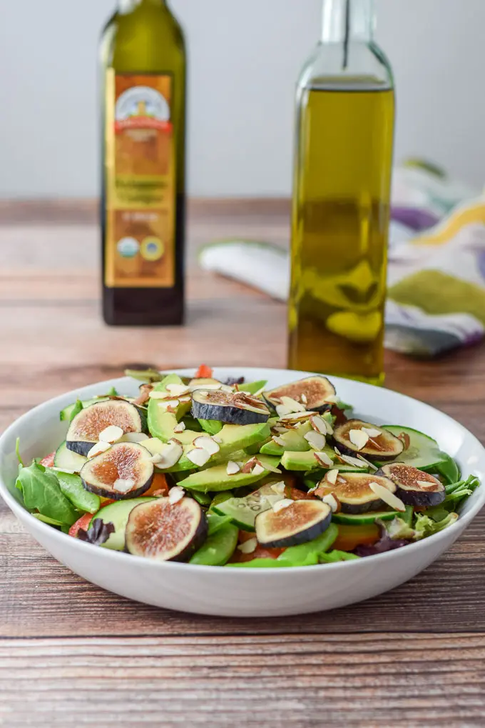 Figs and almond slices added to the salad with oil and balsamic vinegar in the background