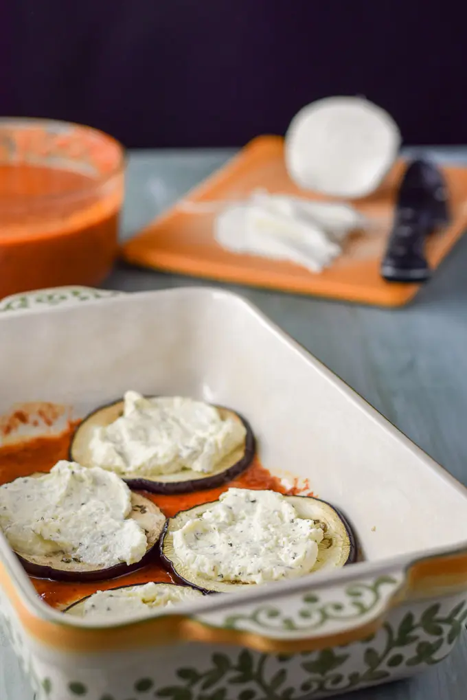 Gravy on the bottom of a baking dish, eggplant on the gravy and ricotta cheese on top of that