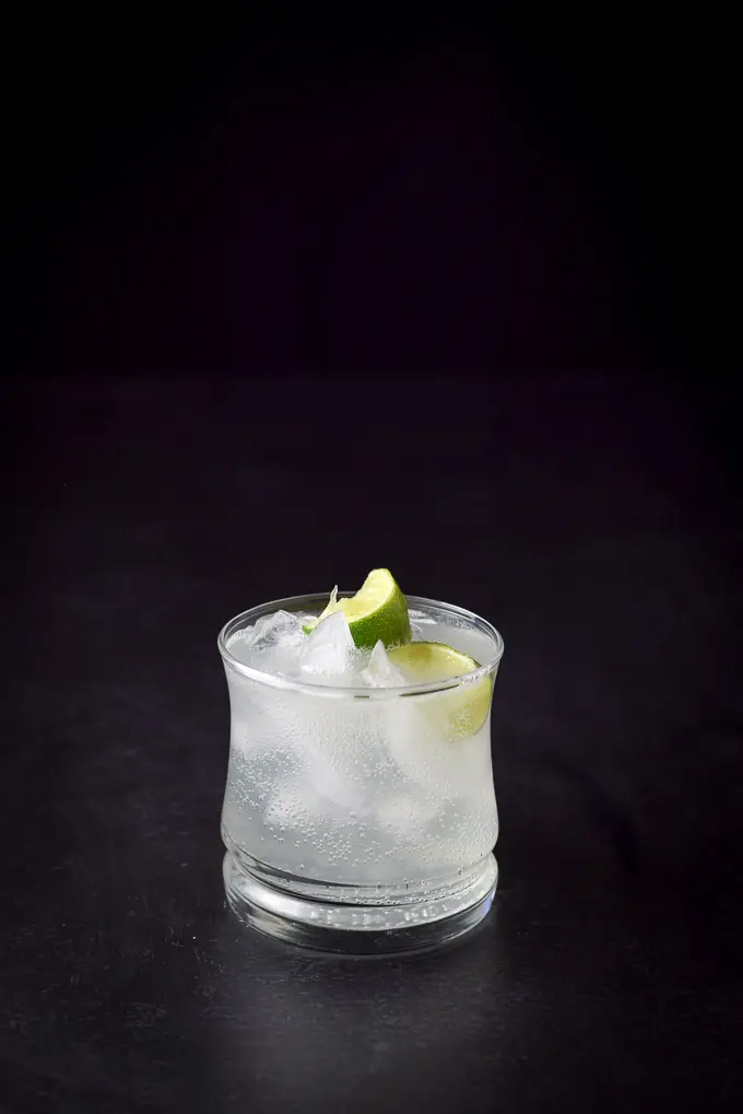 Dark shot of a double old fashioned glass filled with the cocktail with two lime wedges in it