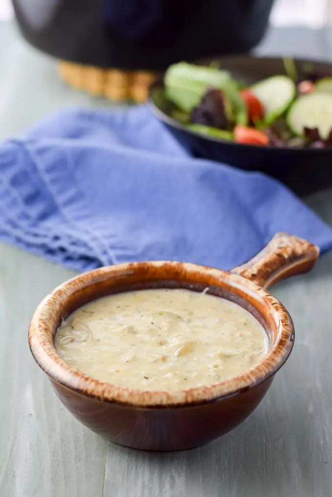 A crock of bisque with a blue napkin, salad and pan in the background